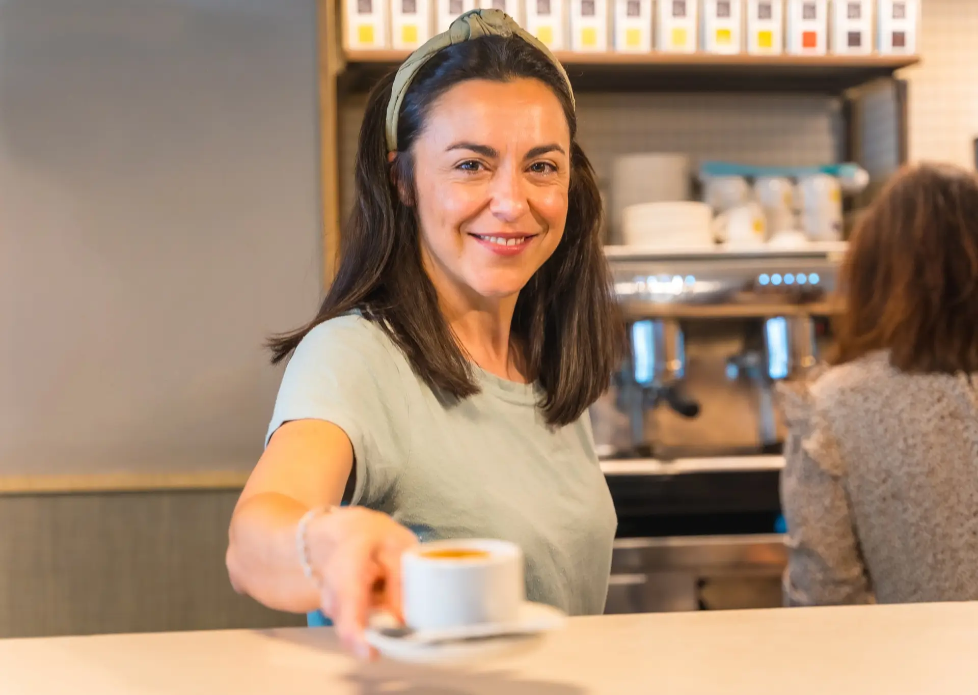 Female cafe owner with a latte in hand, offering the coffee to the customer